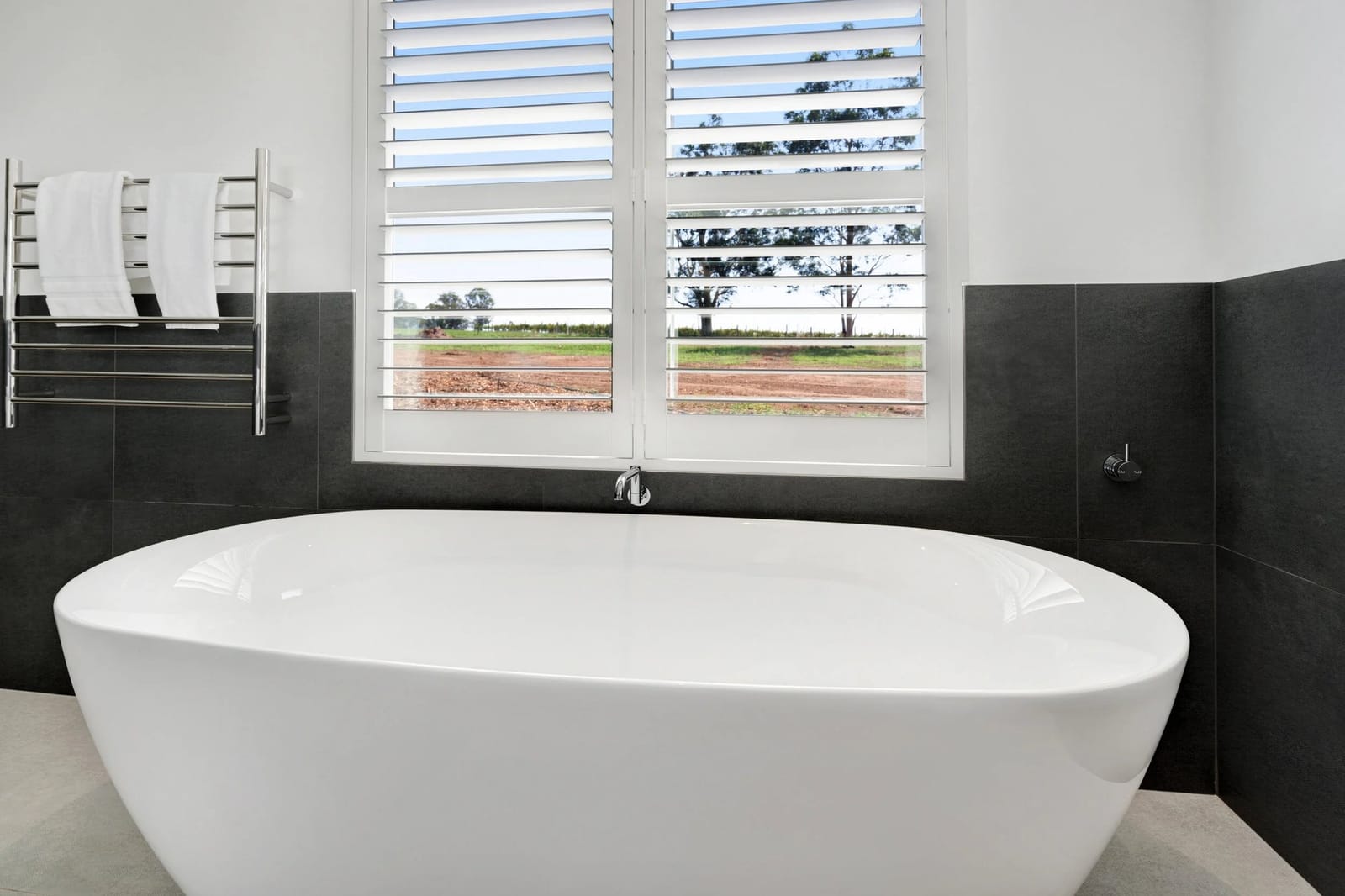 The freestanding bath below plantation shutters looking out to vineyard rows