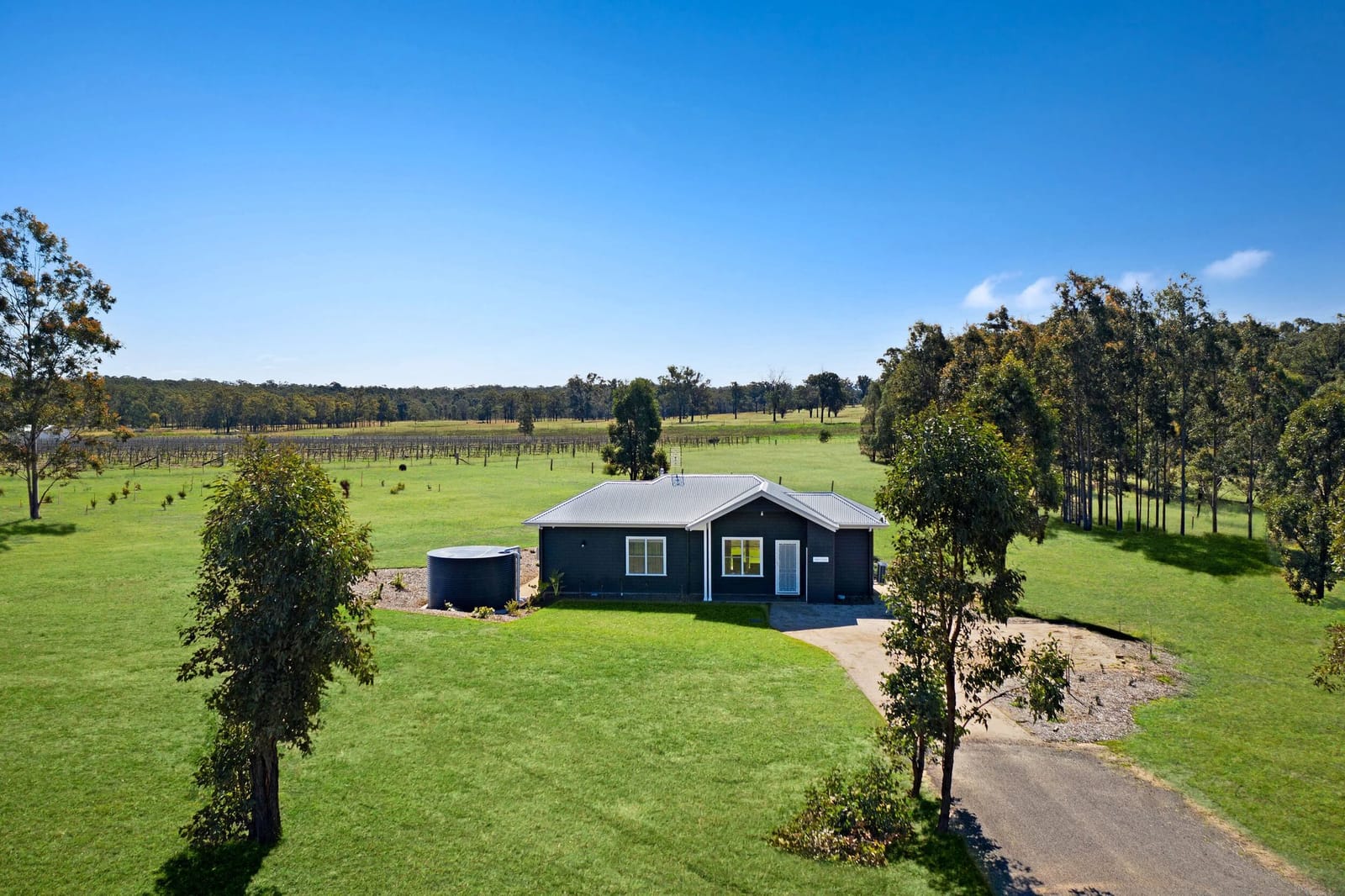 Dark-clad cottage among gum trees and open paddock at Aldora Cottage, Pokolbin, Hunter Valley