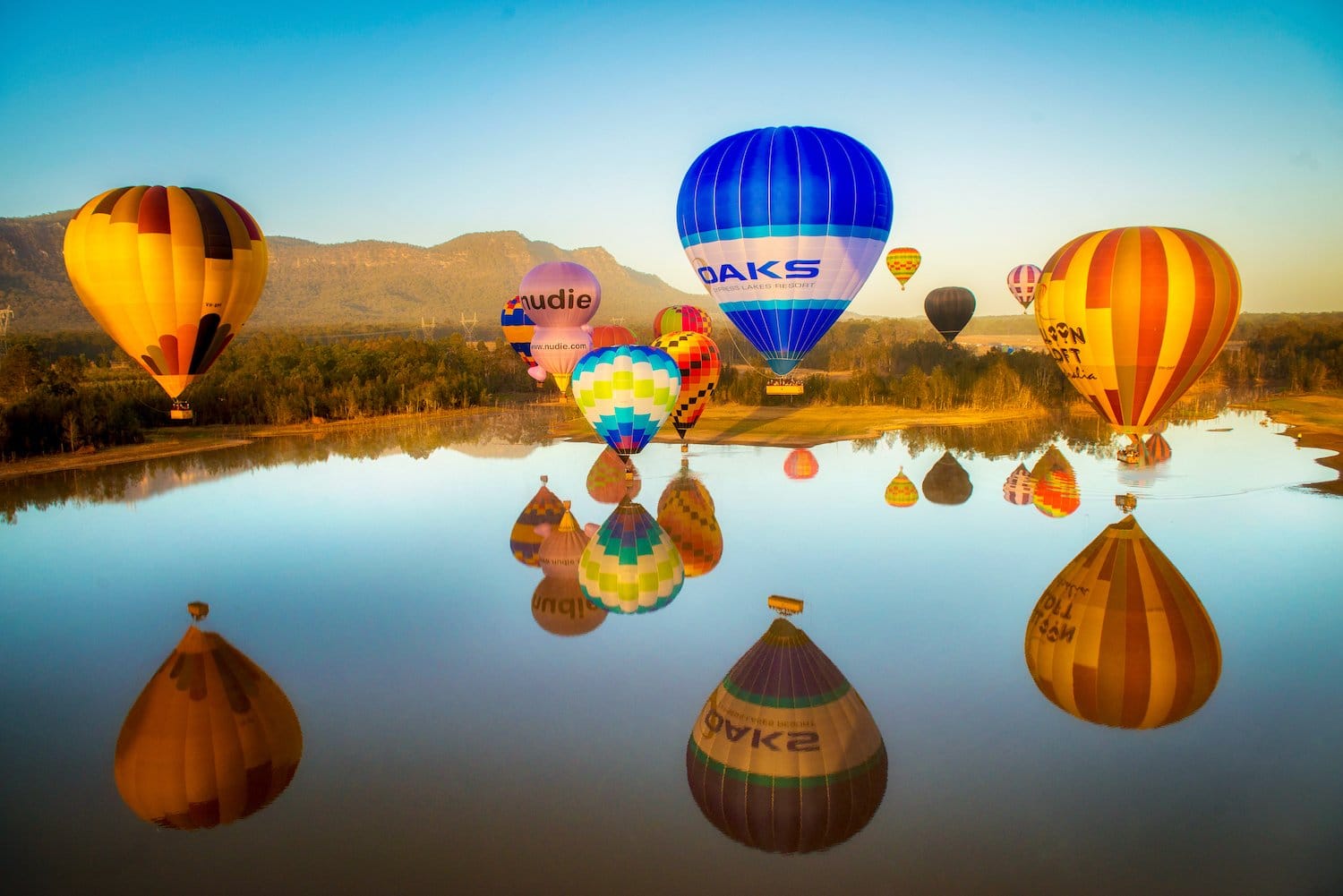 Hot air balloons reflected in calm water at sunrise