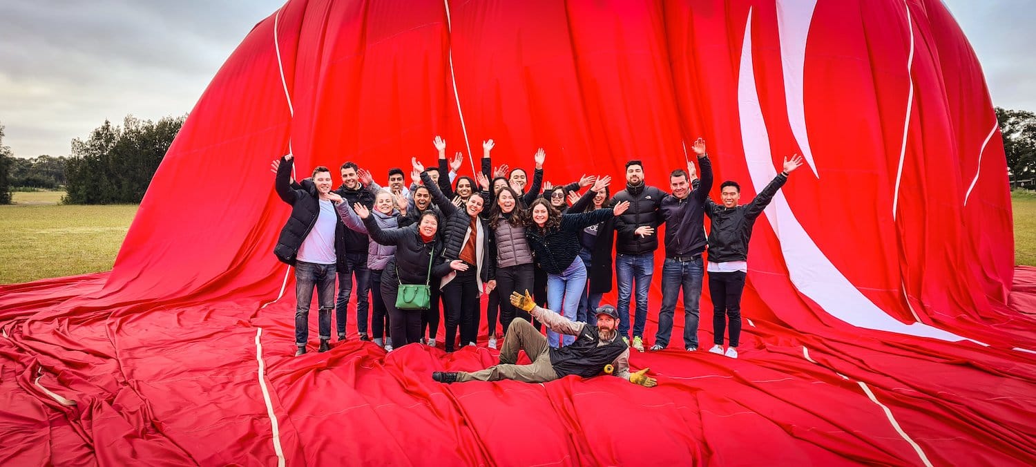 Group of visitors celebrating in front of giant red hot air balloon