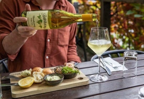 Hands pouring white wine with food on wooden board at Baume Restaurant, Pokolbin, Hunter Valley