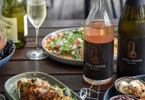 Wine bottles and glasses with plates of food outdoors