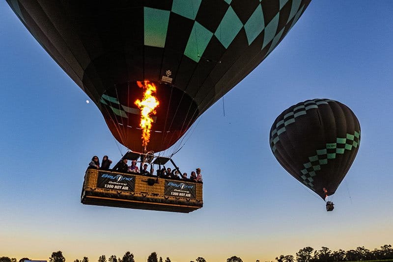 Two balloons at dusk, passengers in the basket as the burner fires
