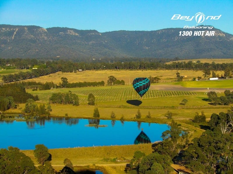 Beyond Ballooning balloon drifting low over vineyards with the Brokenback Range, Pokolbin, Hunter Valley