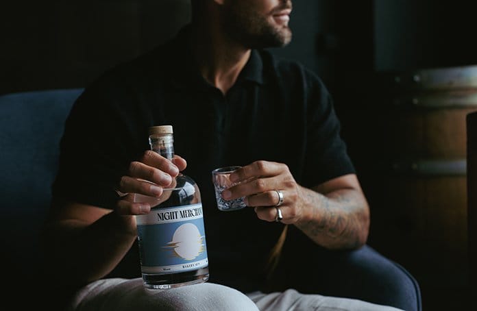Man holding spirit bottle and tasting glass indoors