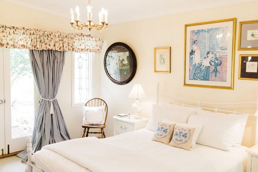 Bedroom with cream bedding, paintings and mirror above bed