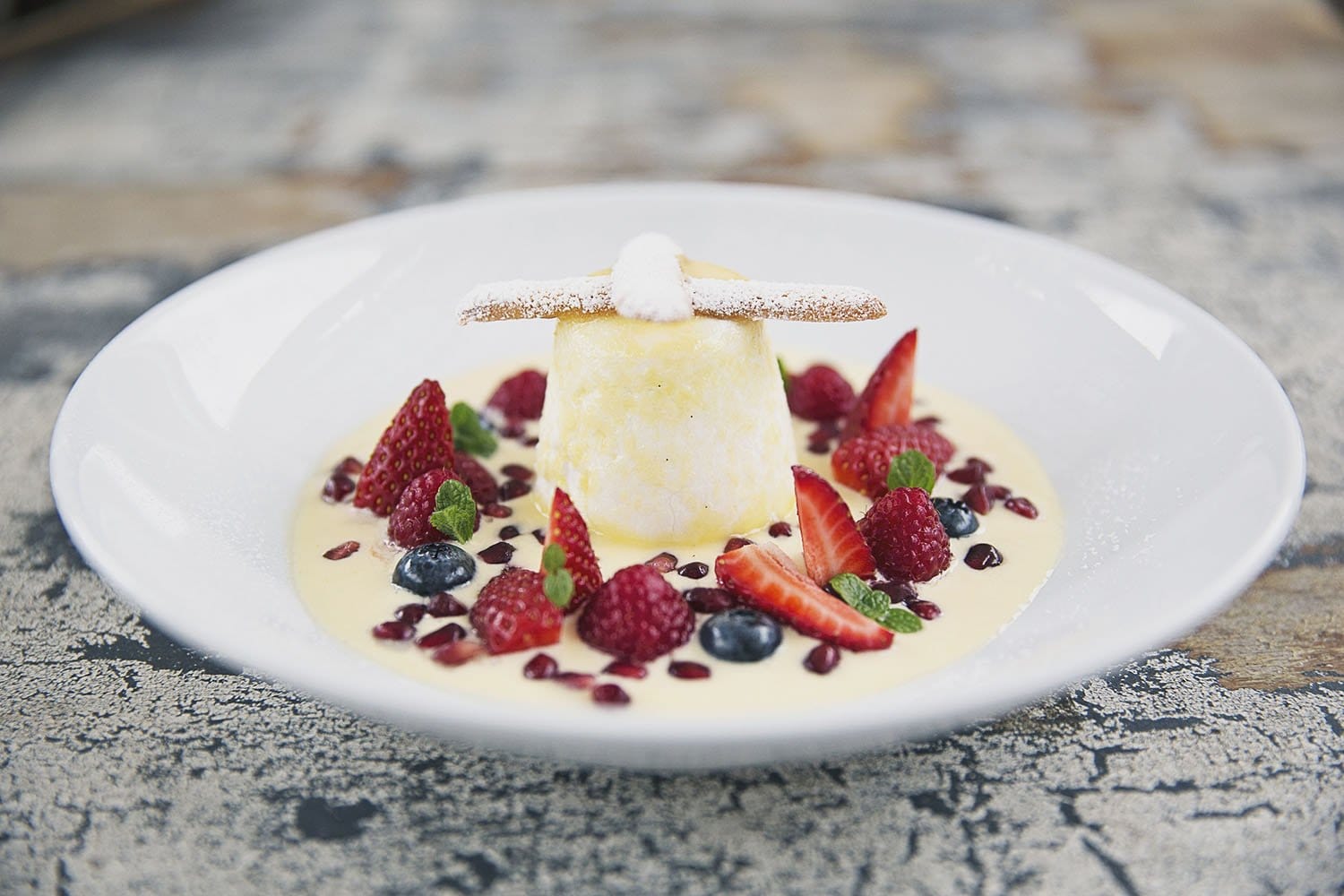 Plated dessert with cream, berries and coulis on white plate