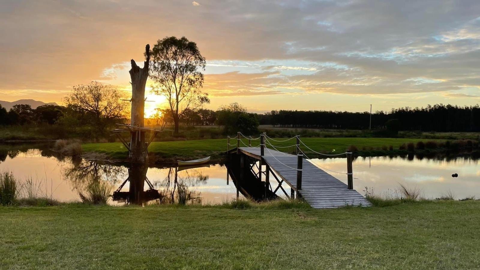 Sunset over the dam and timber jetty at Broken View Estate, with a dog waiting on the boards