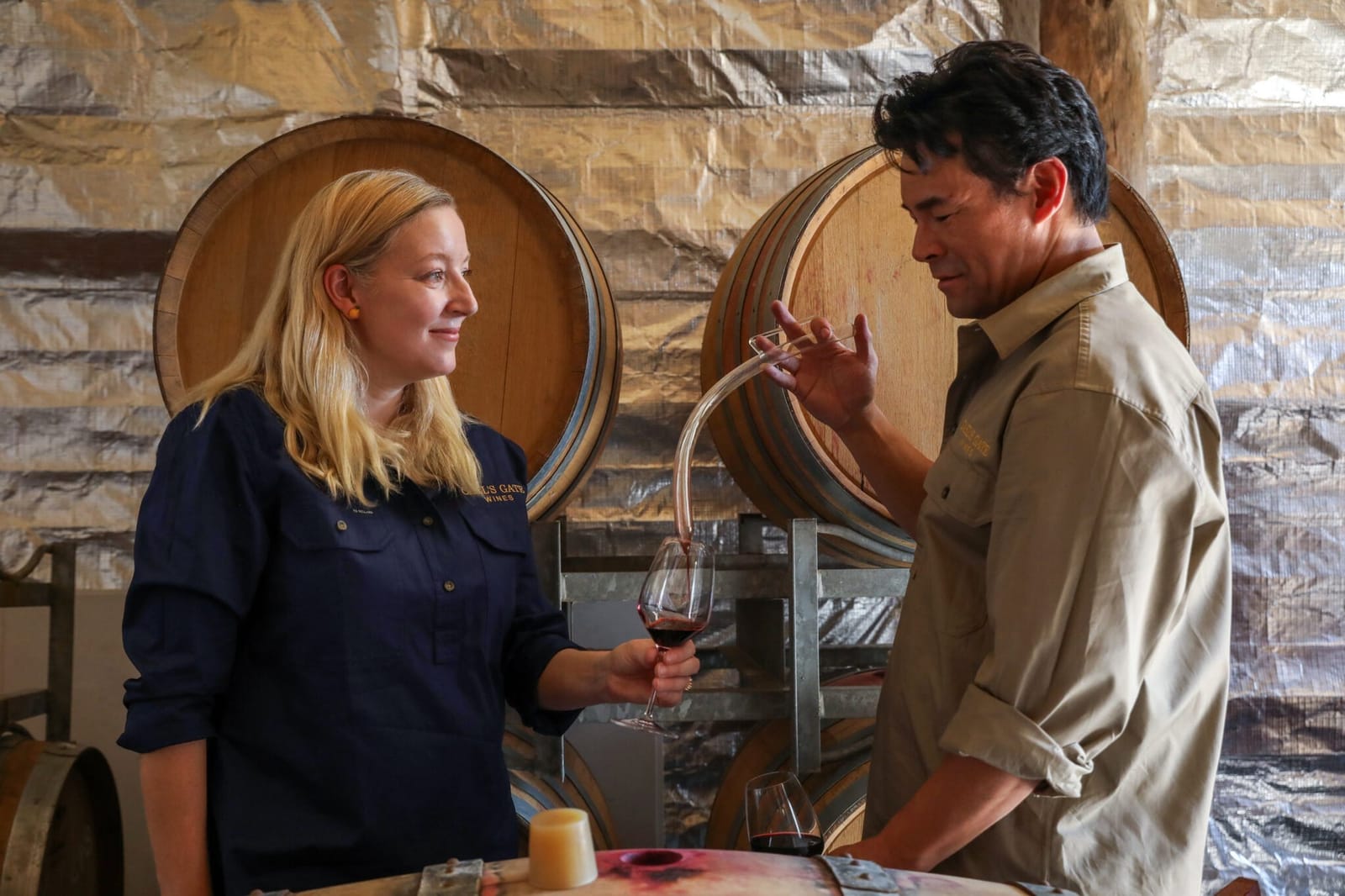Staff pouring wine in barrel room with large oak barrels