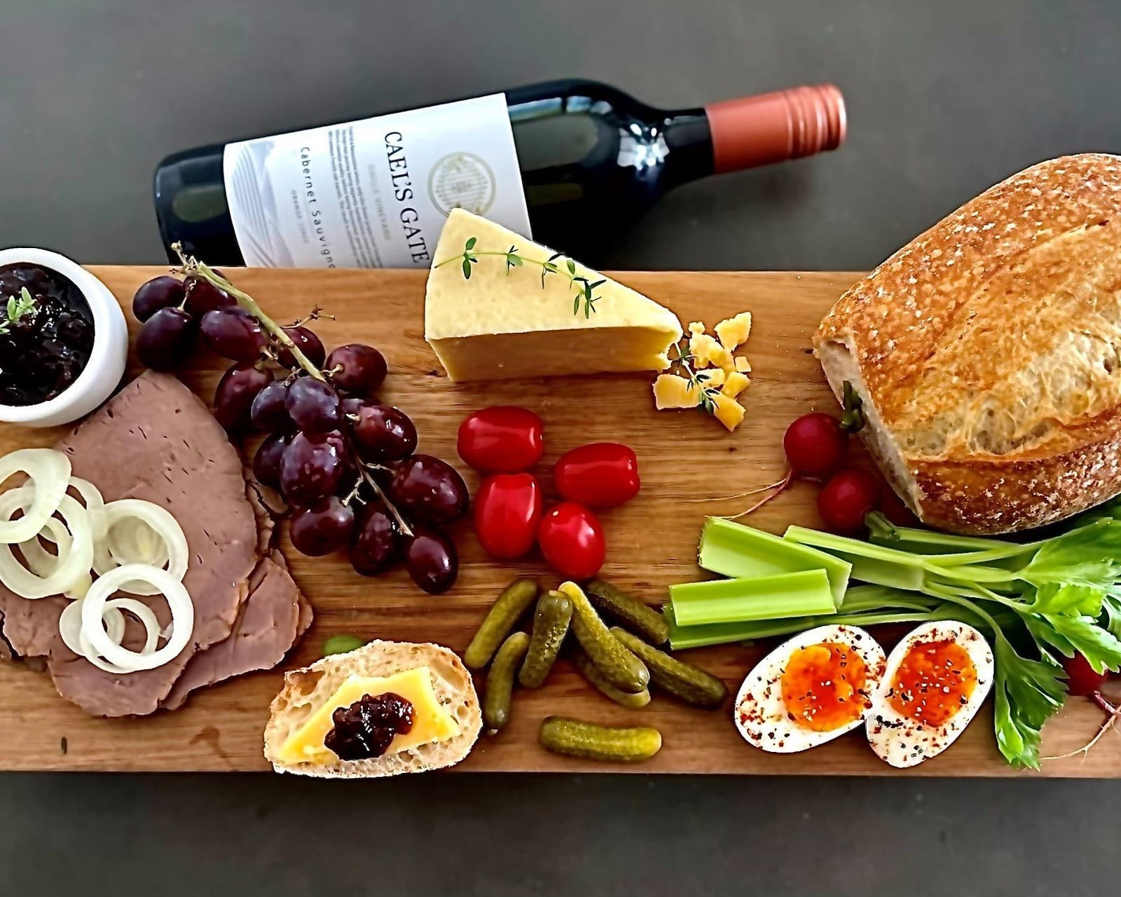 Cheese and charcuterie board with bread, wine and fresh produce