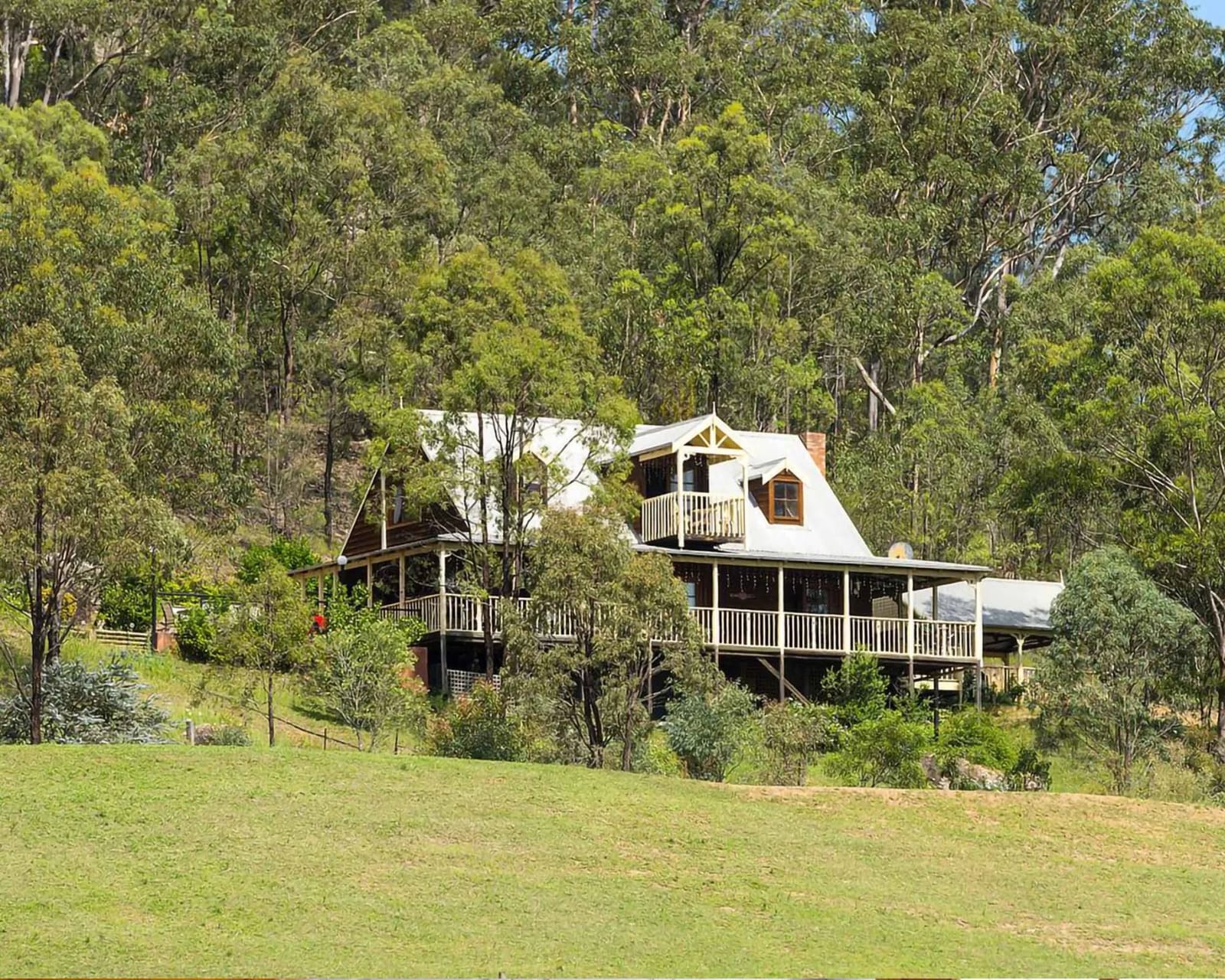 Cant's Cottage and the family loft house seen from the paddock, timber verandas set against bushland.