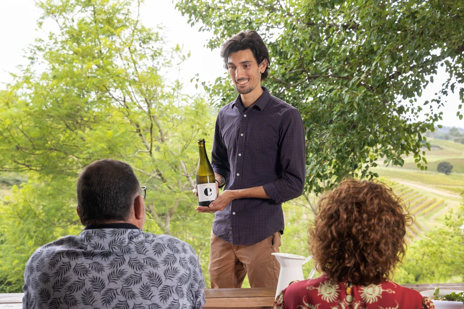 Winemaker presenting bottle to visitors with vineyard views