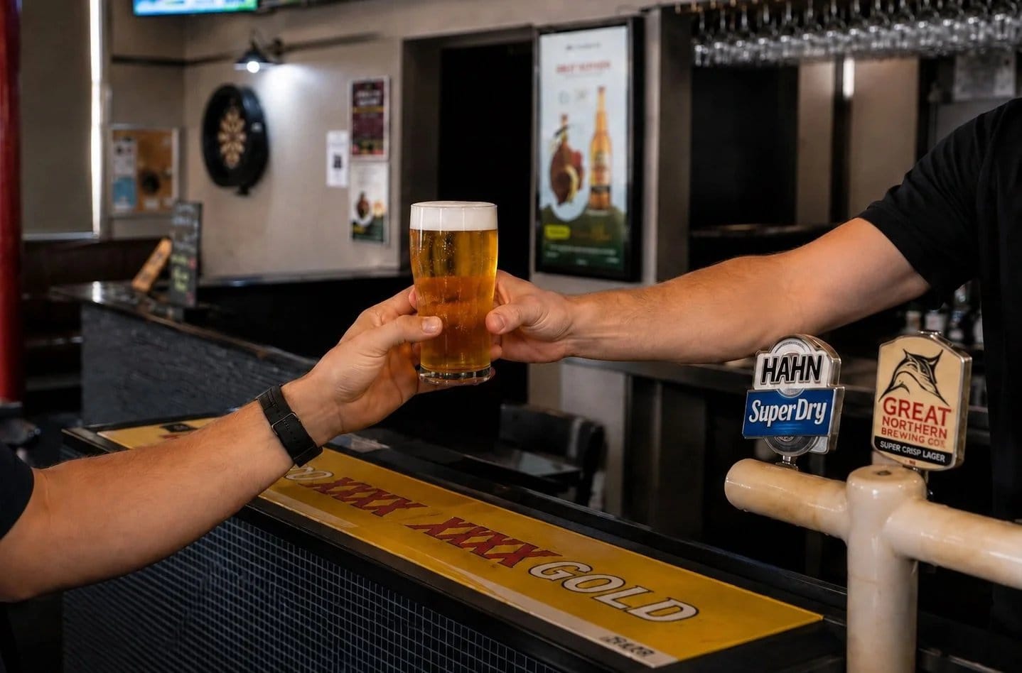 Bartender passing a beer across the bar to a customer at Cessnock Hotel.