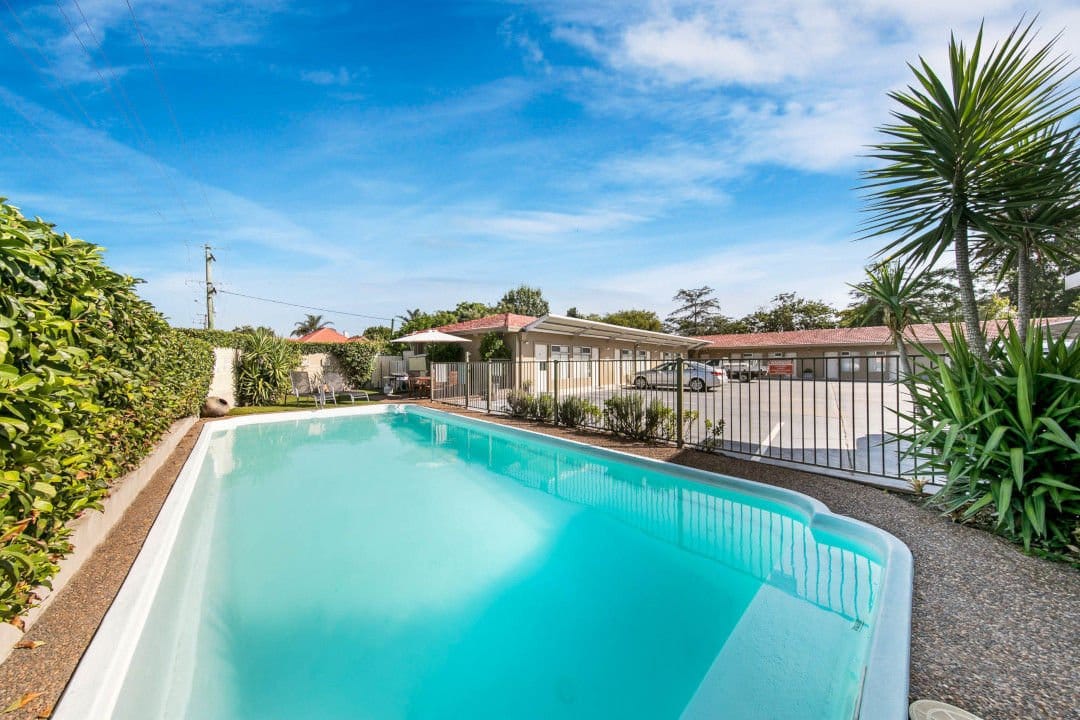 Outdoor swimming pool and motel grounds at Cessnock Motel, fenced by hedges with guest parking behind