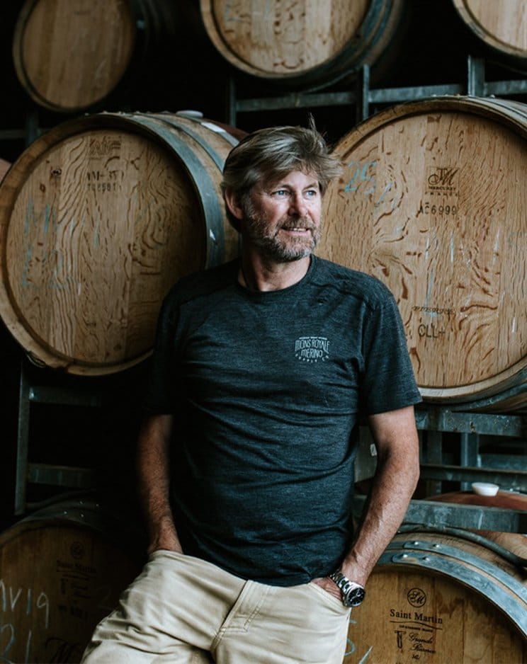 Winemaker in barrel room surrounded by oak wine barrels