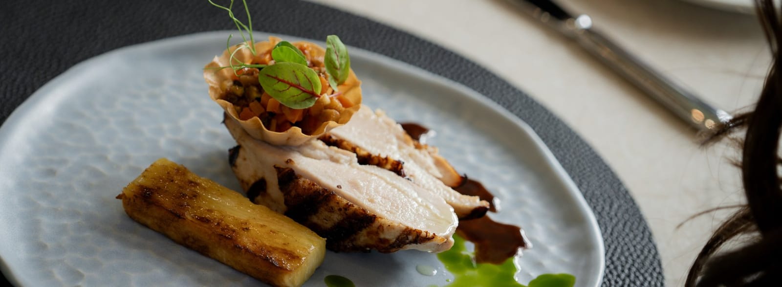 A plated chicken dish with charred pineapple and a filo tart at Legends Restaurant