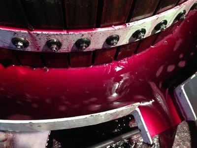 Red wine fermenting inside wooden barrel, showing colour