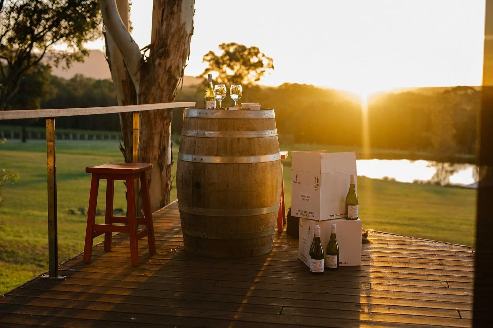 Wine barrel and bottles set on deck with glasses under eucalyptus tree