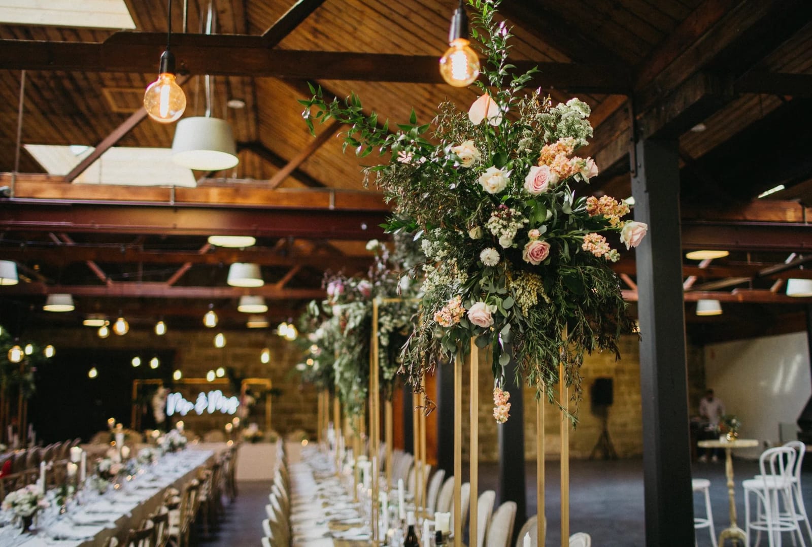 Barn event space with long tables, hanging florals and lighting