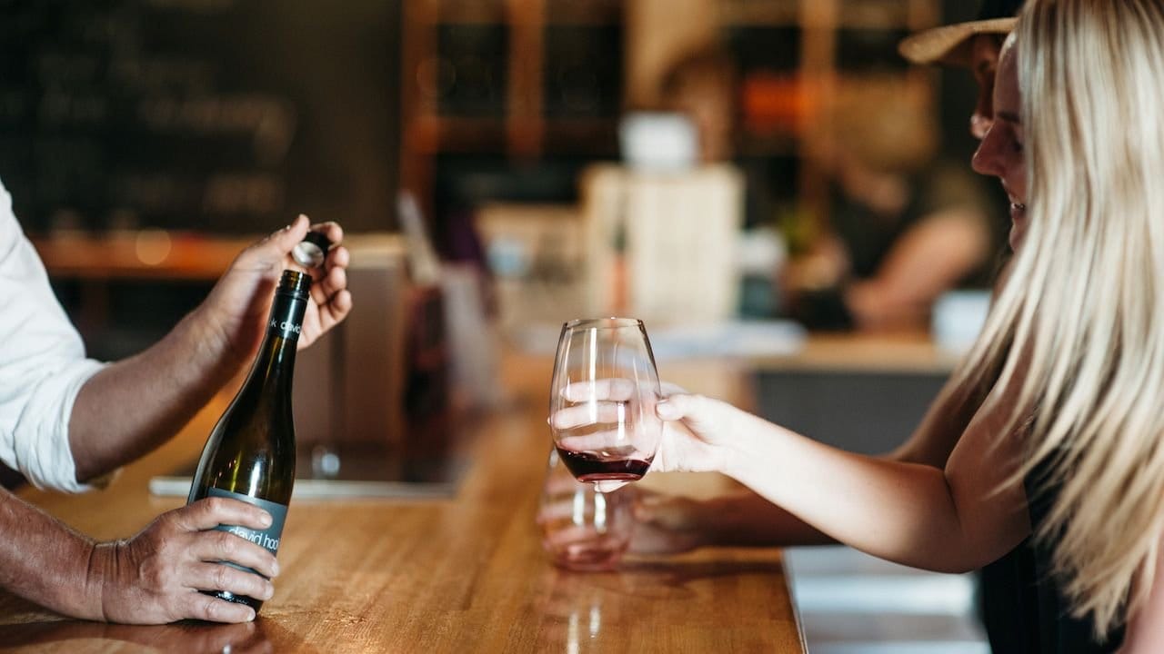 Pouring red wine into glass for woman at cellar door counter