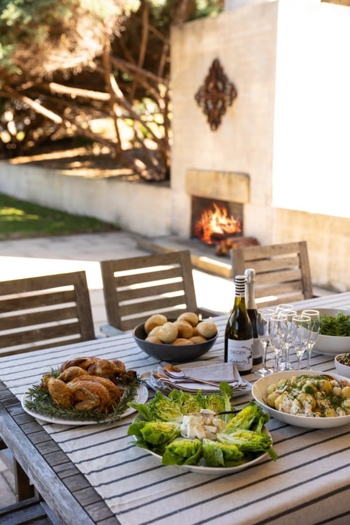 A long outdoor table set for dinner beside a lit fireplace at Degen Estate