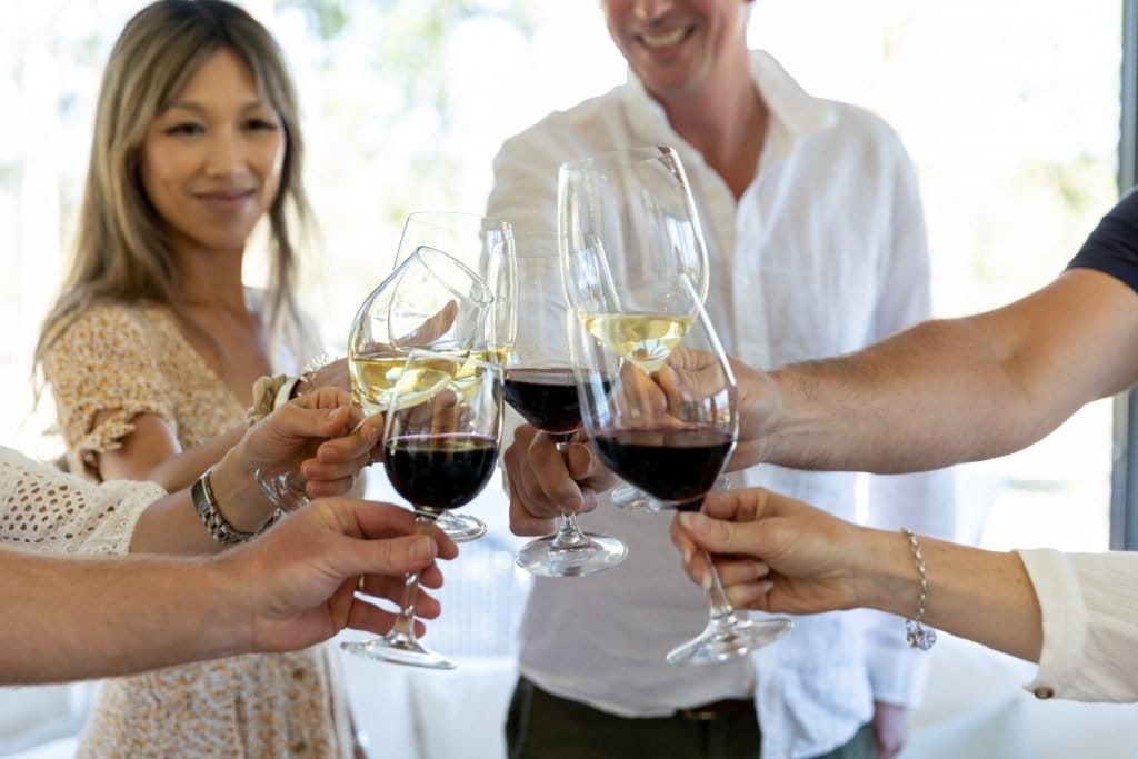 Six hands raising red and white wine glasses in a toast