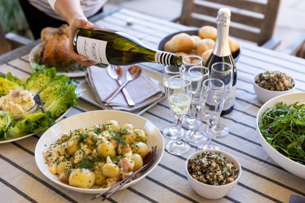 Degen sparkling being poured at an outdoor table set with roast chicken, salads and bread