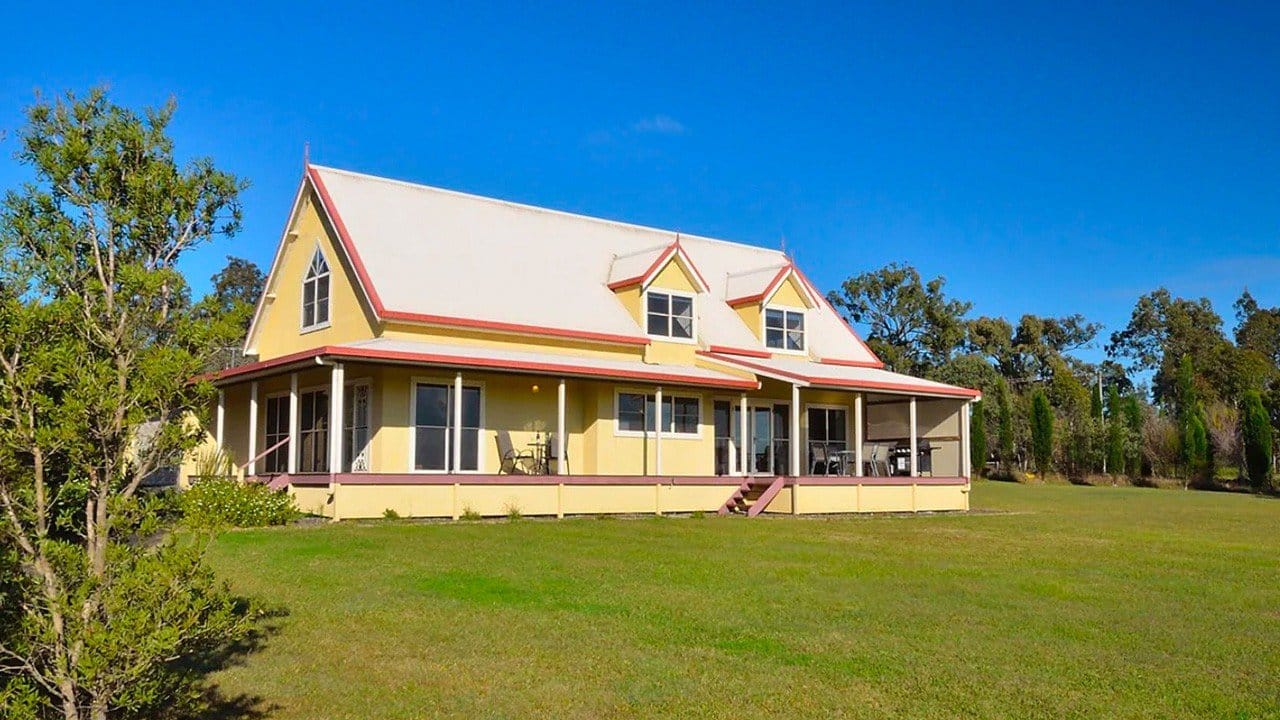 Yellow and red farmhouse building with wrap-around porch and lawn