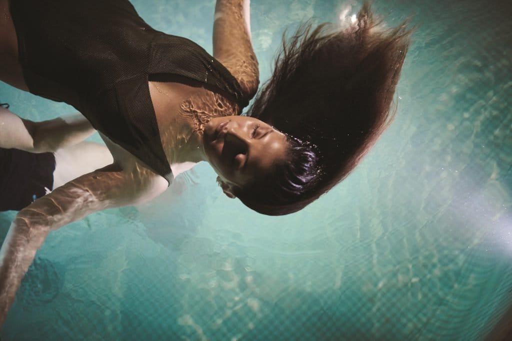 Person floating in turquoise pool water, submerged view