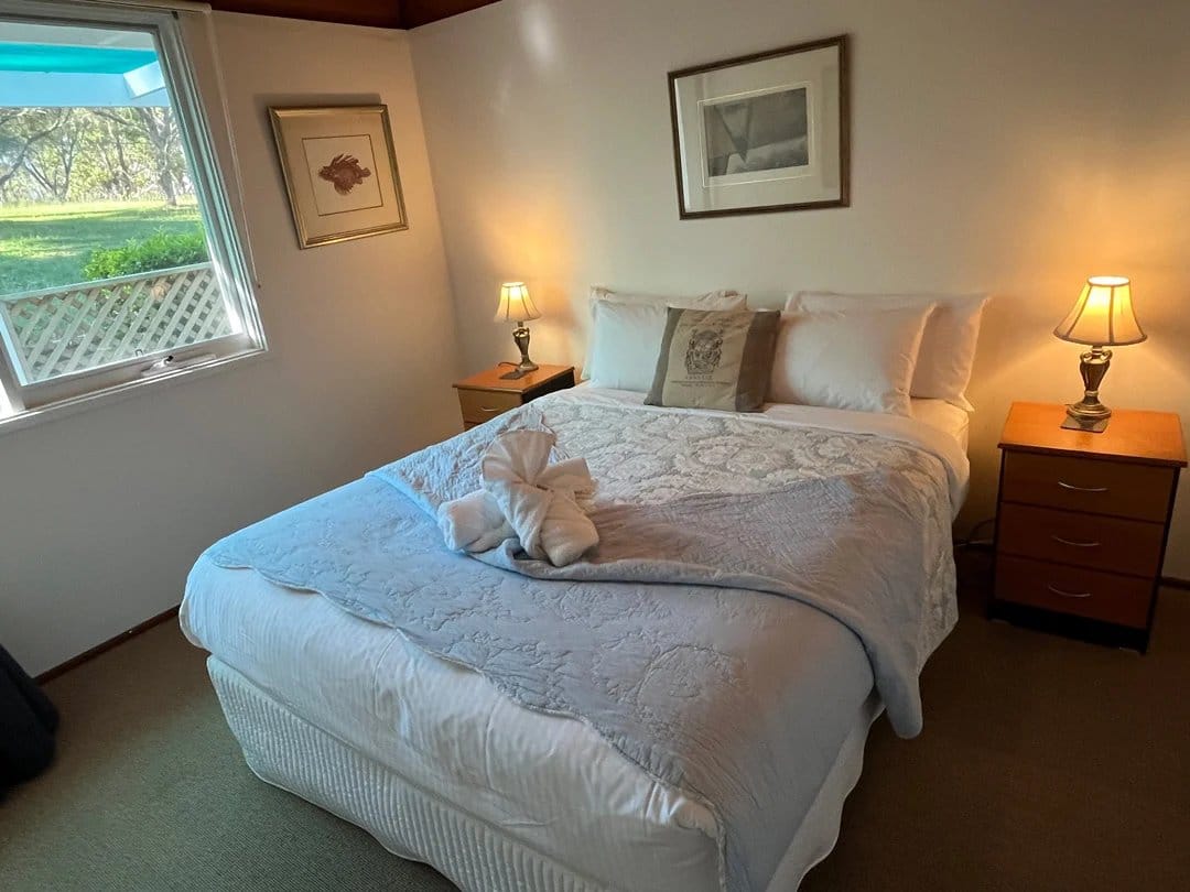 Guest bedroom with queen bed and windows overlooking vineyard gardens