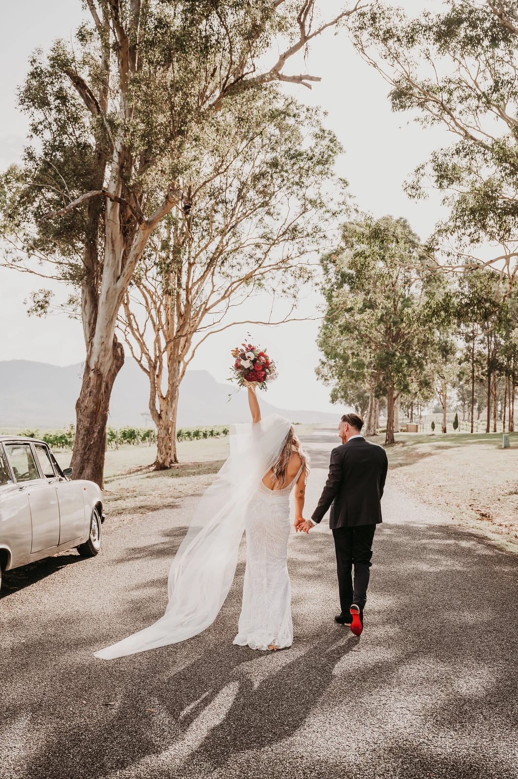 Bride and groom on rural road with vintage car and eucalyptus trees