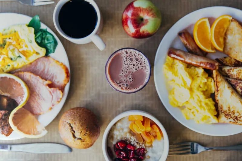 A cooked breakfast spread of eggs, sausages, fruit and coffee viewed from above