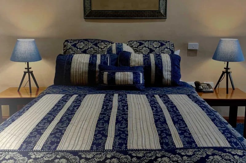 A guest room bed made up with a blue and cream quilted cover, bedside lamps either side