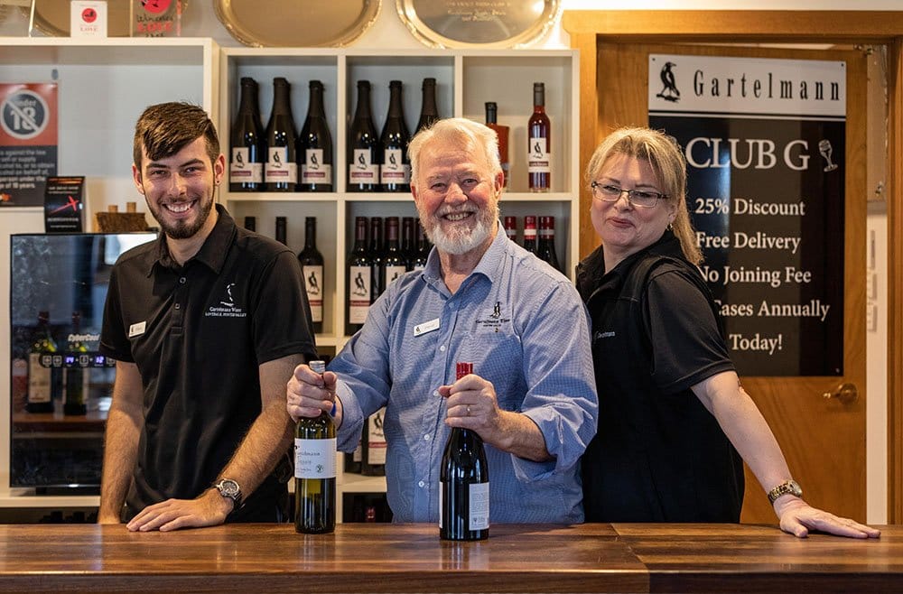Three staff members behind long timber bar with wine bottles displayed above