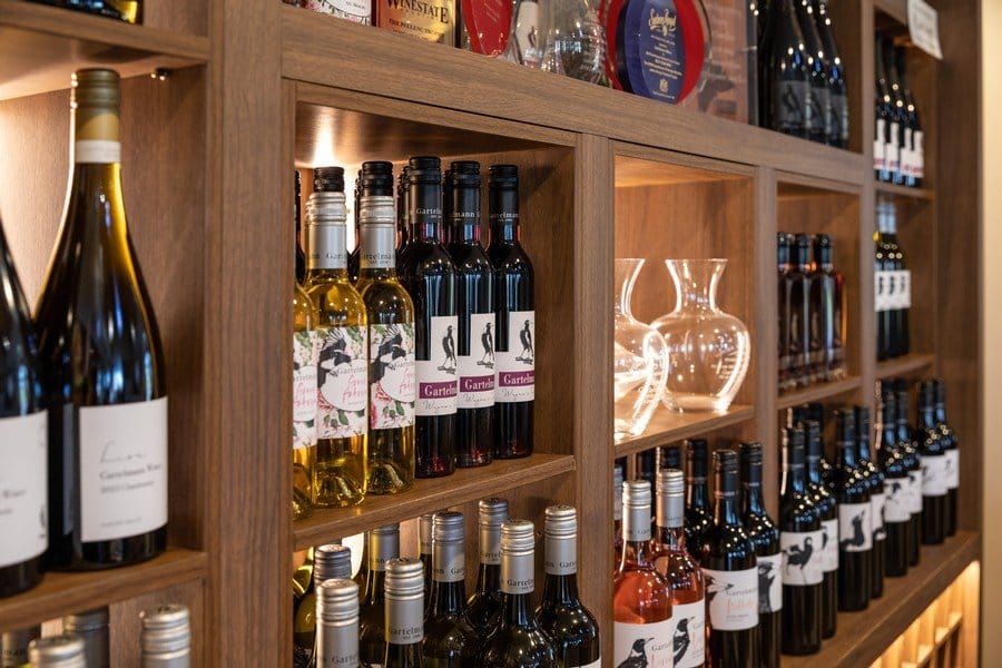 Illuminated wine bottles and glasses on timber shelving with glassware