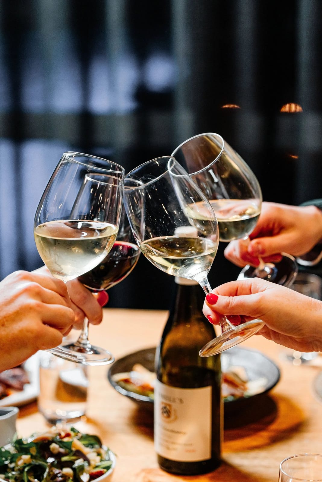 Three wine glasses raised in toast over vineyard dining scene