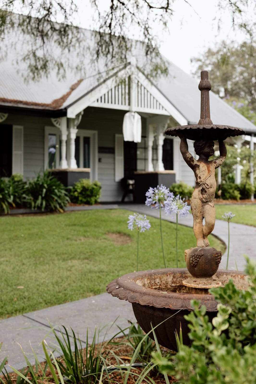 Heritage weatherboard house at Greystone Estate with a garden fountain and lawn in the foreground.