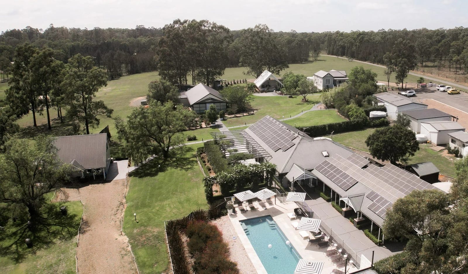 Aerial view of Greystone Estate's pool and heritage buildings surrounded by lawns and trees.