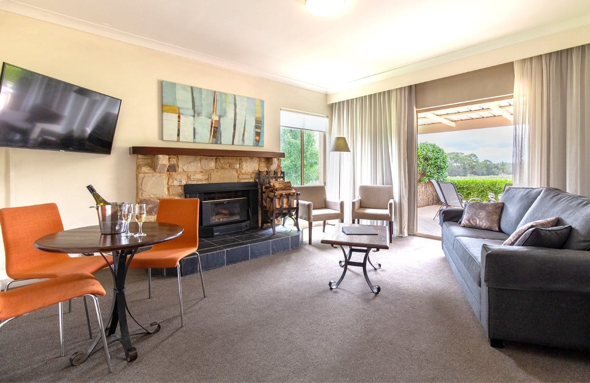 A room lounge with a stone fireplace, sofa and doors open to a terrace over the vines