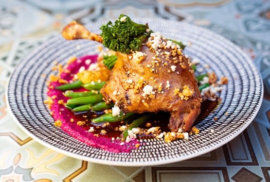 A confit duck leg plated with beans and beetroot purée on a patterned plate