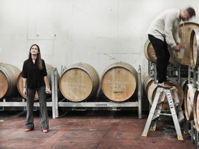 Cellar staff member sampling wine from wooden barrel during production
