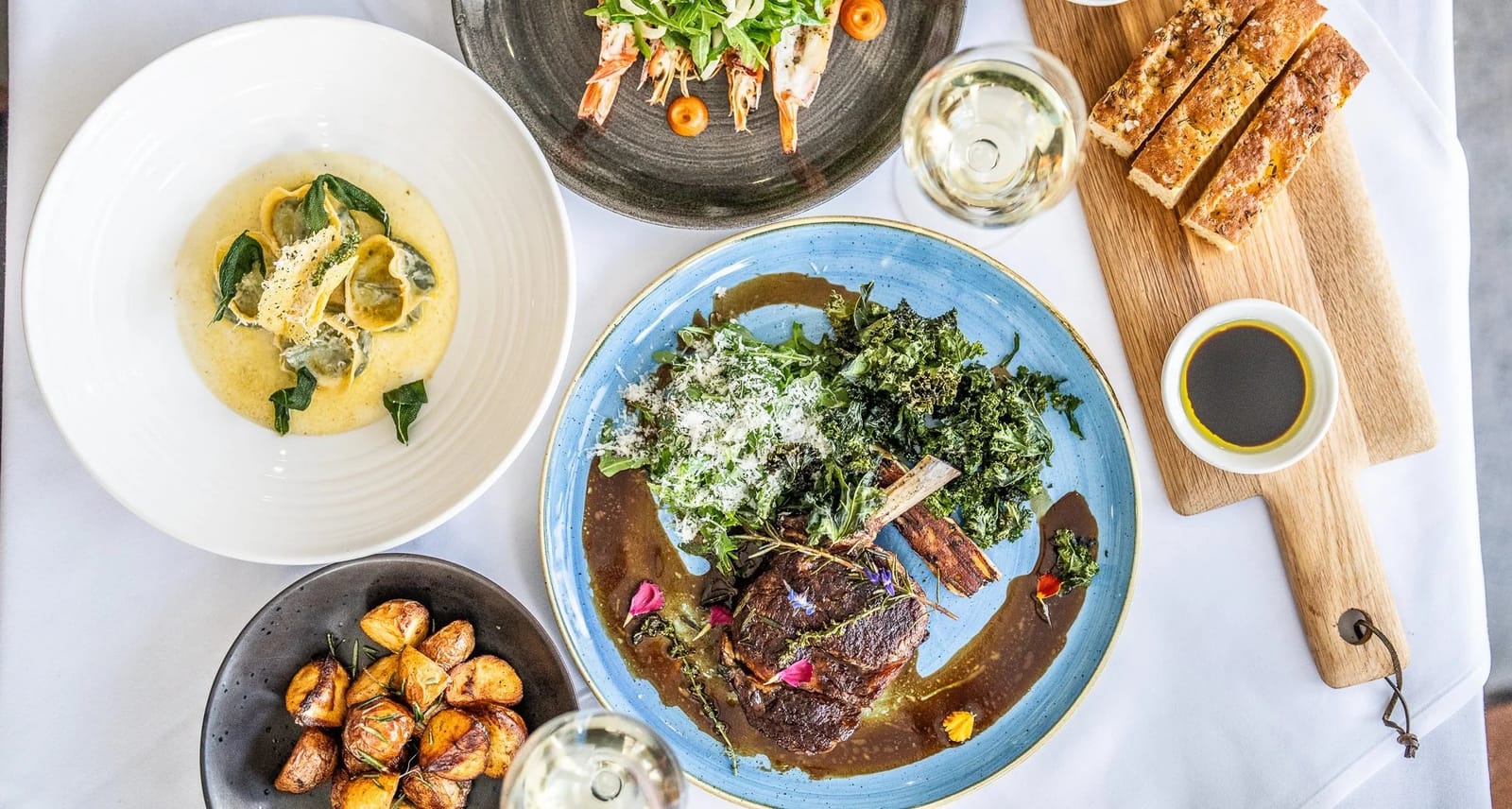 A shared plate of grilled kale, lamb and toasted bread with a glass of red wine on a table at Harvest.