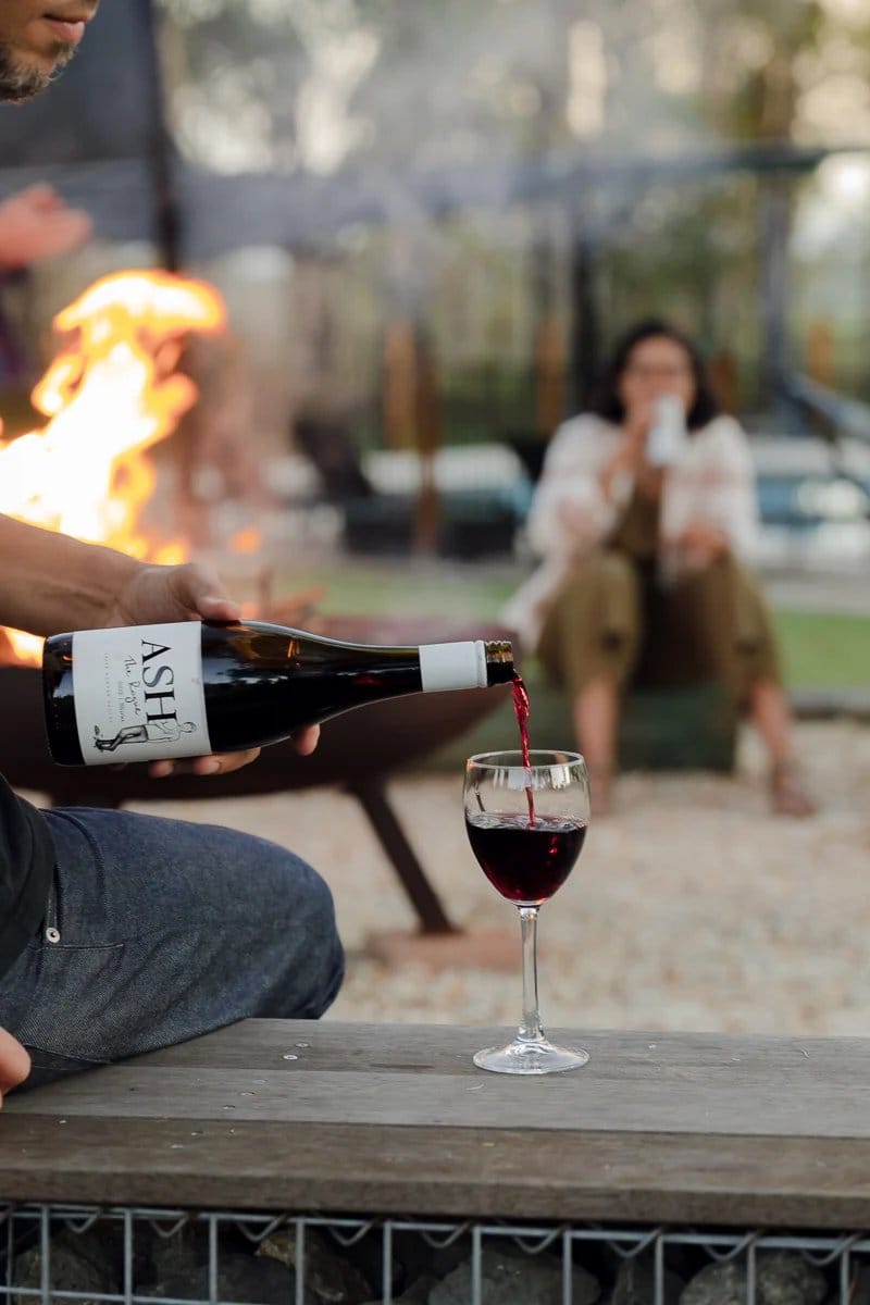 Red wine being poured outdoors by fire pit with gathering guests