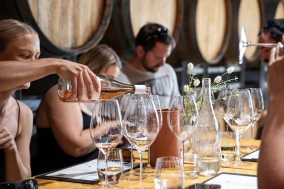 Sommelier pouring wine into tasting glasses with oak barrels behind