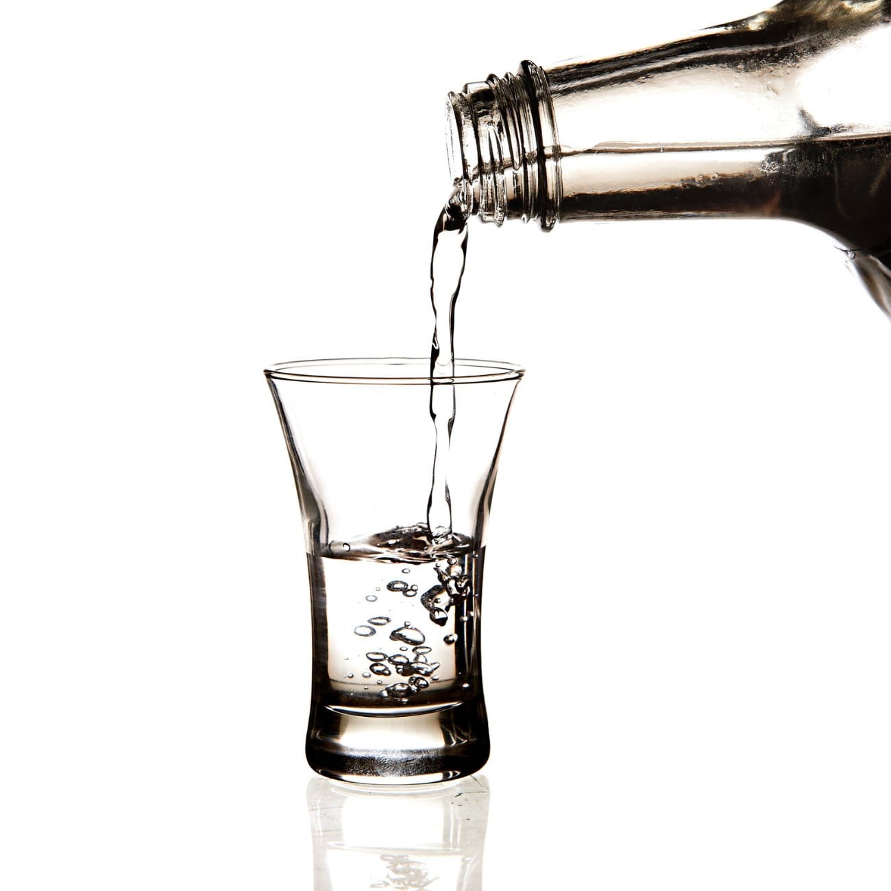 Spirit pouring from bottle into shot glass, close up on white