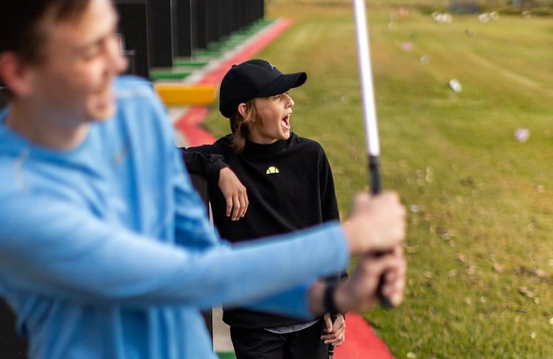Two players laughing at the Aqua Golf hitting bays with balls scattered across the fairway