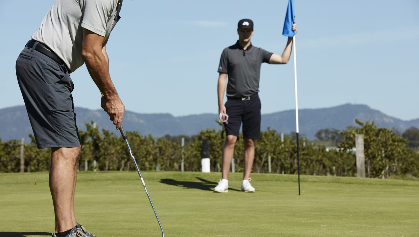 Two golfers putting on a green with hills in the background at Hunter Valley Golf Club.