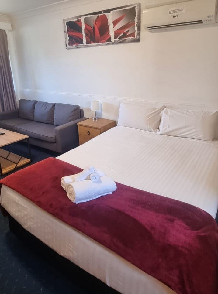 Made-up queen bed in a guest room at Hunter Valley Motel, with a lounge and wall-mounted air conditioning unit.
