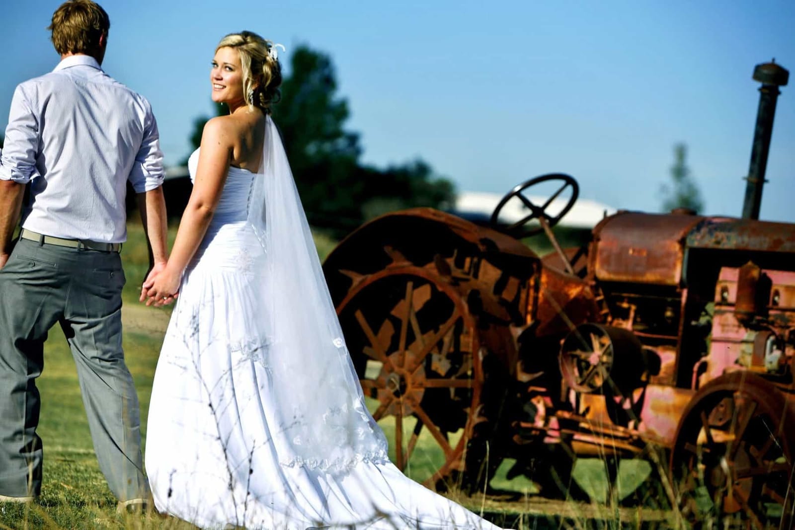 Bride and groom posing beside weathered vintage farm machinery outdoors