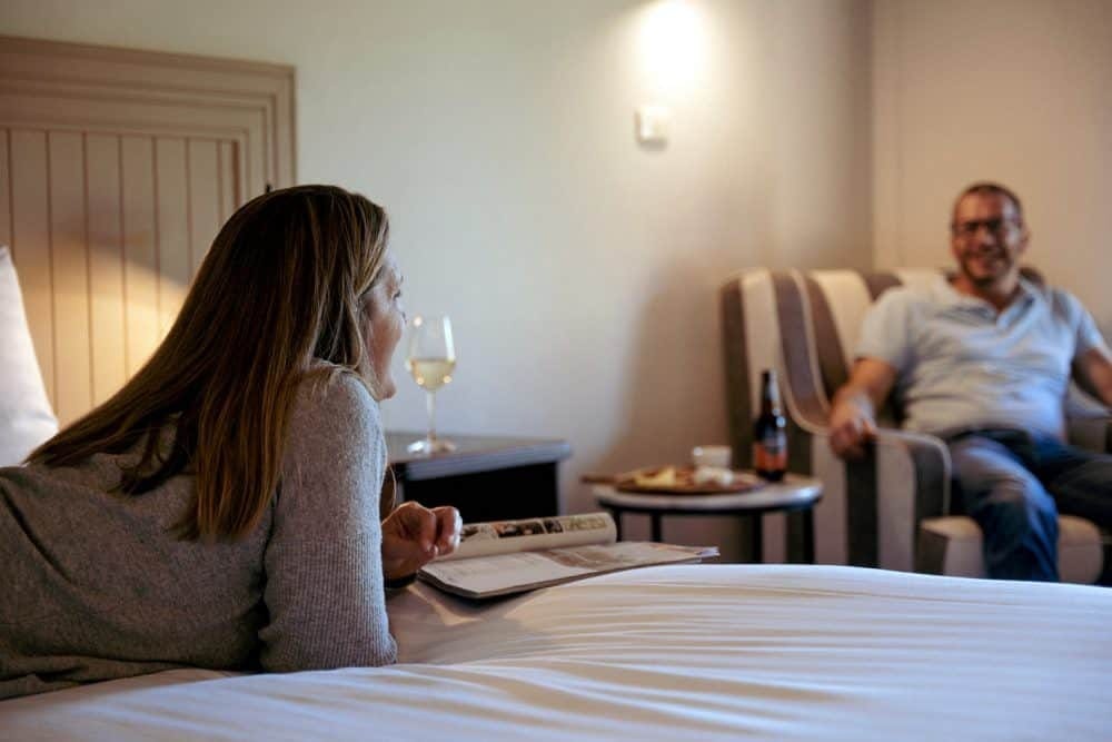Guest bedroom with woman enjoying wine, man relaxing in background